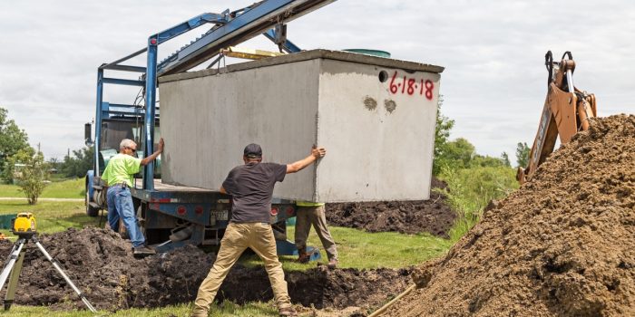 A Septic Installation Crew Hoists A Concrete Septic Tank Between Mounds Of Excavated Dirt