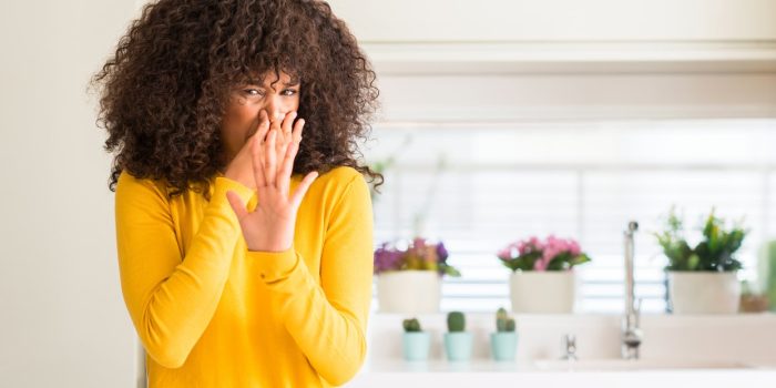 A Woman Wearing A Yellow Sweater In The Kitchen Smelling Something Stinky And Disgusting