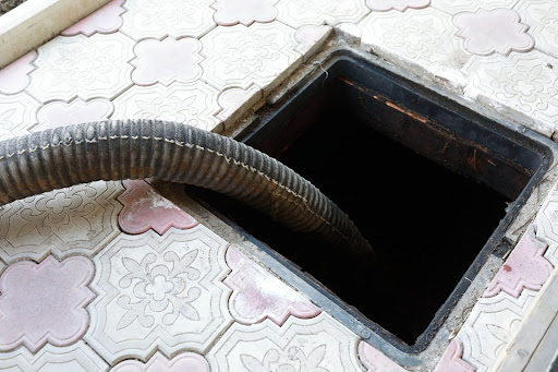 An Open Septic Tank With A Large Hose Inside Surrounded By Tile Flooring.