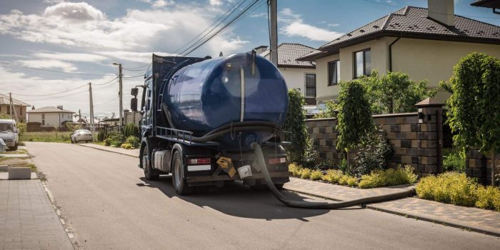 A Sewage Tank Truck Parked In Front Of A House Representing Septic Tank Cleaning.